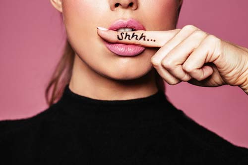 closeup of pretty womans face with finger in her mouth and Shhh... written on her finger