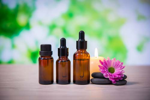 Three essential oil bottles next to a candle and pink flower