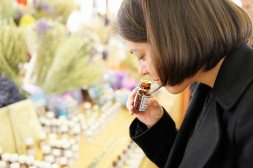 Woman with brown hair sniffing an essential oil bottle.