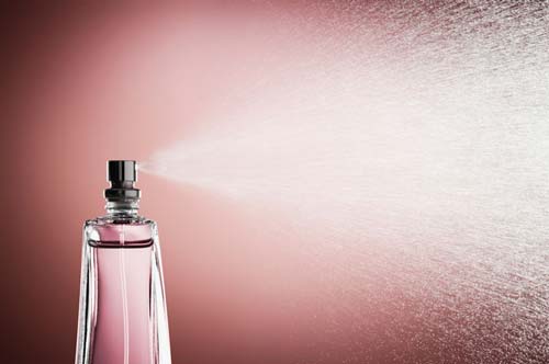 Glass bottle of perfume spraying mist against pink background