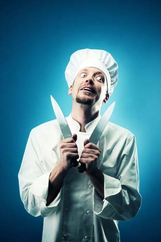 Chef with a crazy look on his face, holding a knife.