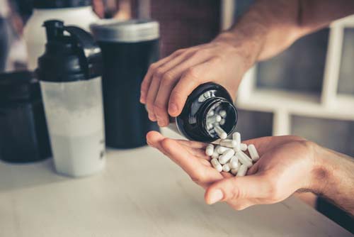 Man pouring supplements into his hand with sport nutrition shake in the background